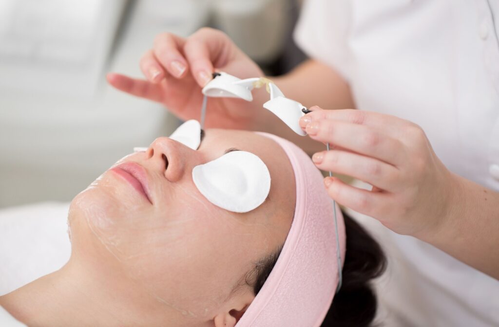 An optometrist placing a white protective shield over a patient's eyes before IPL treatment for dry eyes.