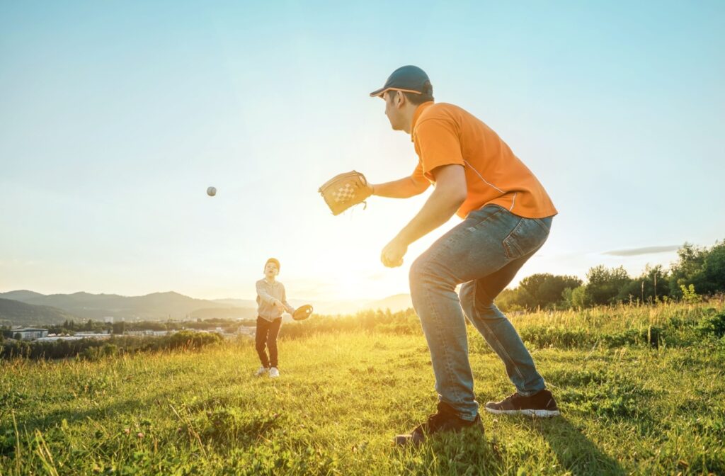 A parent and child playing catch in a field on a sunny day.